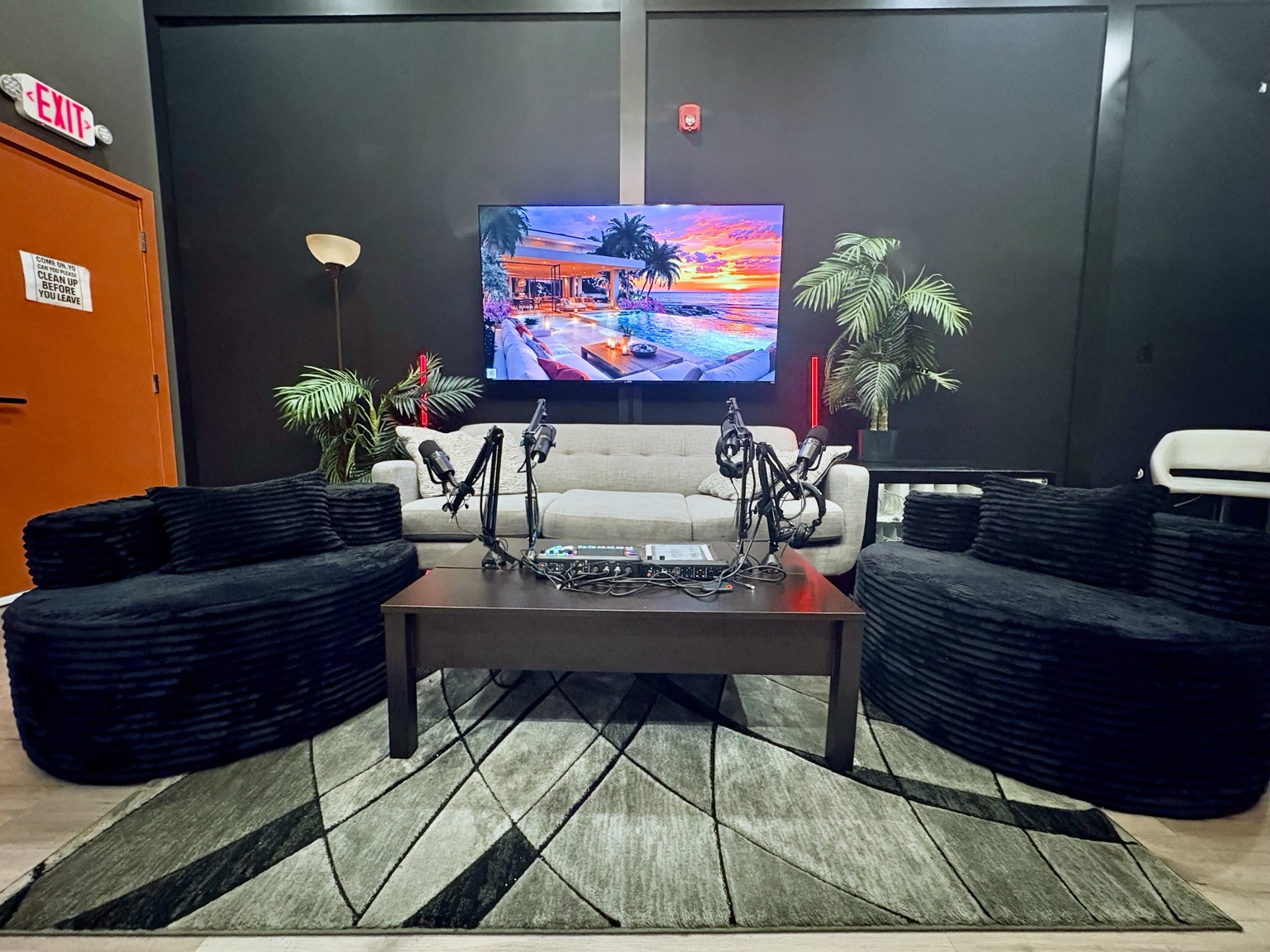 Front view of the Sound Twist podcast set with four microphones, a beige sofa, two black chairs, and a wall-mounted TV