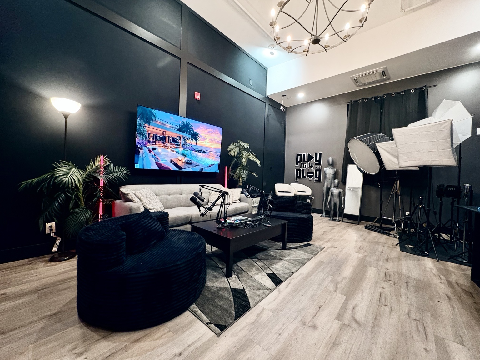 Wide view of the Sound Twist podcast set with sofa, black chairs, four microphones, wall-mounted TV, and studio lighting